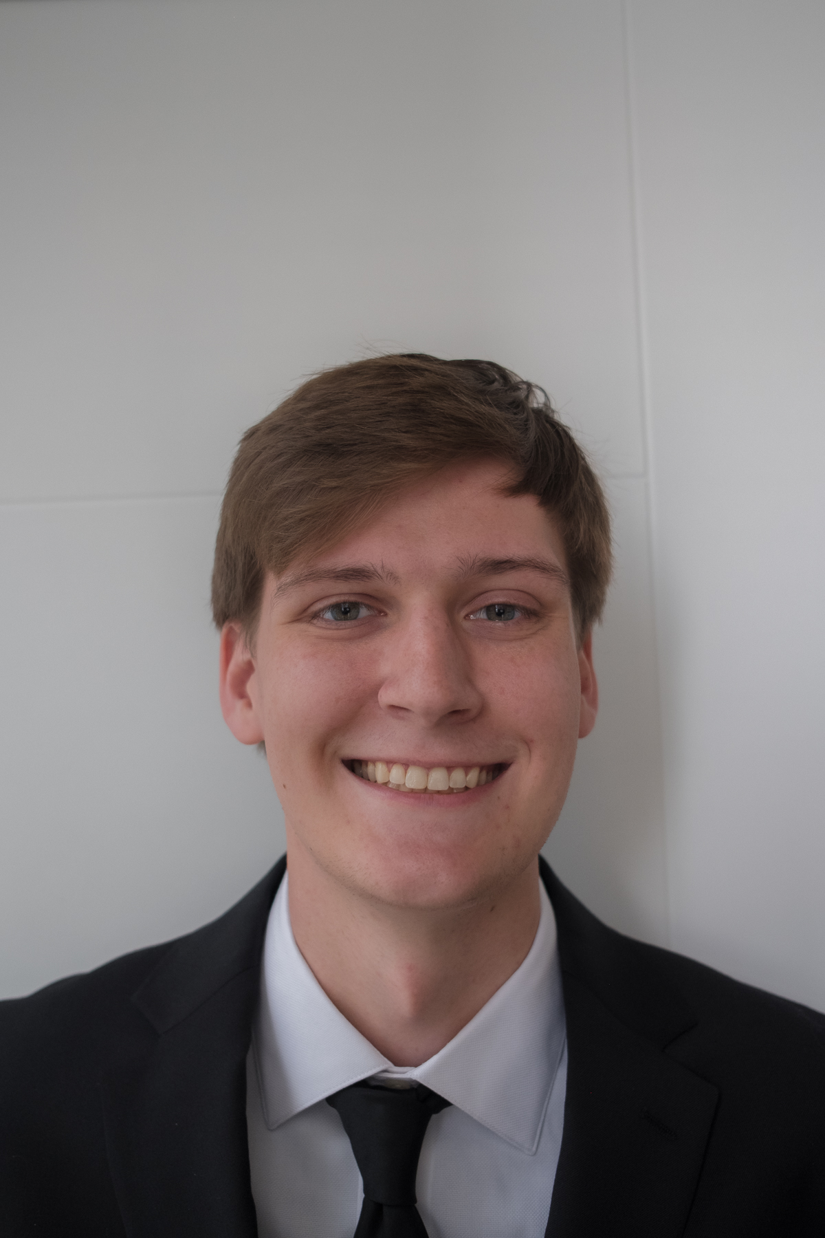 Professional headshot with black suit and tie against a white backdrop